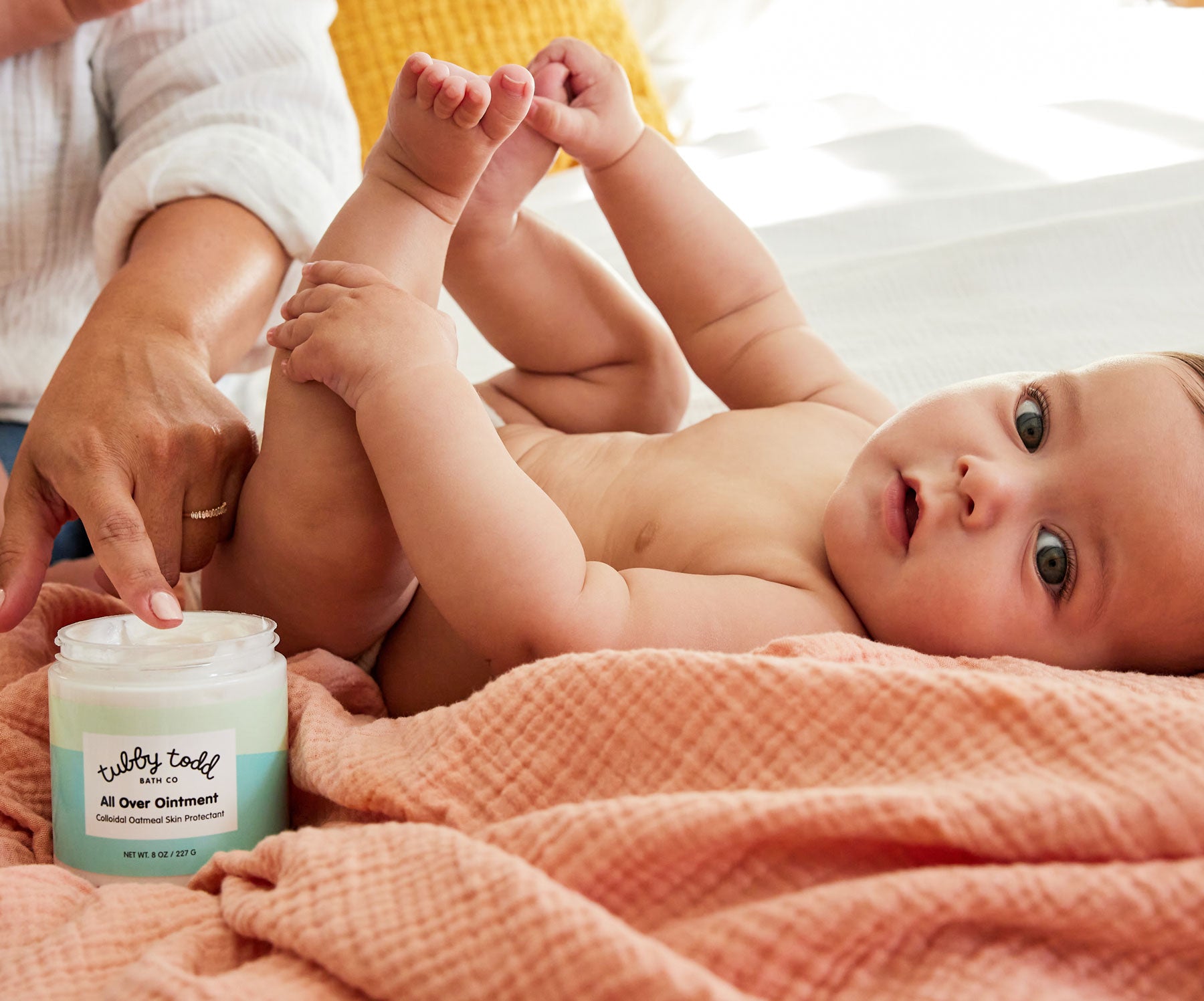 Mama applying All Over Ointment on her baby who's looking at the camera